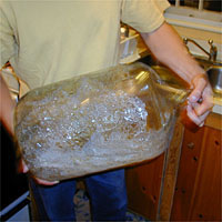 Person holding a large, glass carboy containing suds in a kitchen.